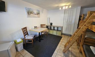 A simple room with two chairs and a table. In the background, there is a loft bed and a TV.
