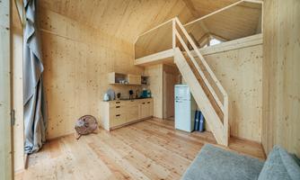 A modern wooden house with open spaces and a wooden staircase. The decor is simple and functional, with large windows that let in plenty of light.