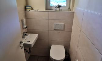 A small, modern bathroom with a toilet and a sink. The window brings in daylight and offers a view outside.