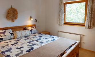 A cozy bedroom with a large bed and modern wood details. The window lets in plenty of daylight and offers a view of greenery.
