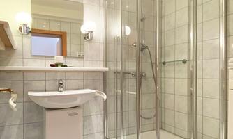 A modern bathroom with a shower and sink. The walls are tiled, and there is a large mirror with lighting.