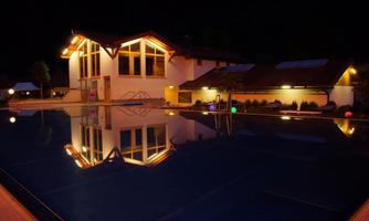 A swimming pool at night with a illuminated building in the background. The reflective lights create a romantic atmosphere.