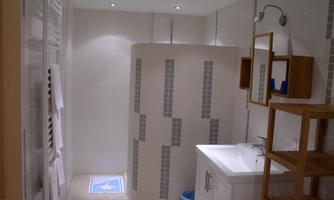 A modern bathroom with a shower cubicle and a sink. The walls are tiled in light colors and there are wooden shelves for extra storage.