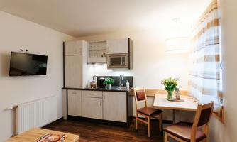 A modern kitchen with a dining area and a TV on the wall. The room is bright and cheerfully designed.