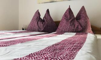 A cozy bedroom with a bed and decorative pillows. The bedding features an appealing pattern in shades of red and white.