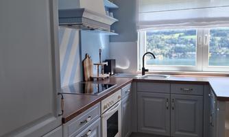 A modern kitchen with gray cabinets and a wooden floor. The window provides plenty of daylight and a view outside.