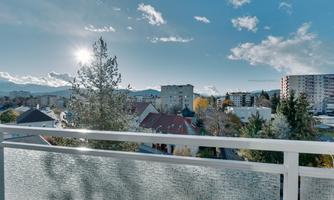 A sunny view of a city landscape with modern buildings and trees. The sky is blue with some clouds and the sun is shining.
