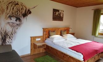 A cozy bedroom with wooden furniture and a large bed. On the wall, there is a picture of a Highland cattle.