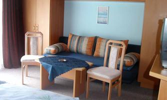 A cozy living area with a blue sofa and colorful cushions. The room is bright and cheerfully furnished with wooden furniture.