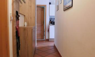 A narrow hallway with a wooden cupboard and an open door in the background. The walls are painted light, and the floor is fitted with terracotta tiles.