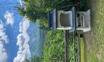 A grill outdoors stands in front of a beautiful mountain landscape. The surroundings are green and peaceful.