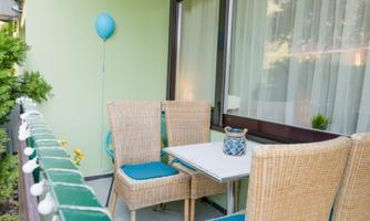 A cozy balcony with two rattan chairs and a small table. A blue balloon and plants give the space a pleasant atmosphere.