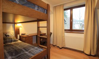 A cozy room with a bunk bed and a desk. The window lets in plenty of daylight and offers a view outside.