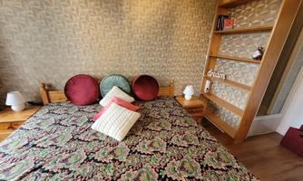 A cozy bedroom with a wooden bed and colorful pillows. On the wall, there is a bookshelf and a decorative lettering with the word "dream".