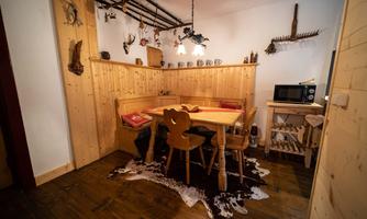 A rustic dining area with wooden furniture and a round table. Decorative elements hang on the walls, and there is a fur on the floor.