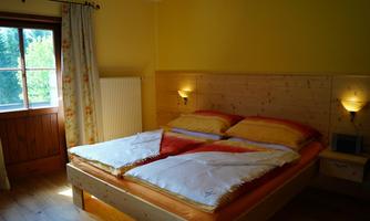 A cozy bedroom with a large double bed and bright bedding. The walls are painted in warm shades of yellow, and a window lets in natural light.