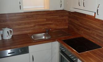 A modern kitchen with glossy white cabinets and a wooden surface. It is equipped with a sink, a stove, and an oven.