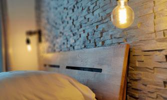 A modern bedroom with a wooden bed and a stone wall. The warm lights create a cozy atmosphere.