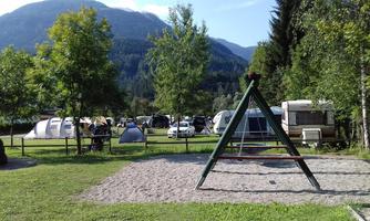 A beautiful campsite with caravans and tents. In the foreground, there is a swing on a sandy area.