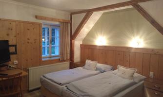 A cozy room with two single beds and wooden elements. There is a table, a television, and plenty of natural light from a window.