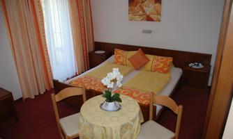 A cozy room with two single beds, orange pillows, and a small table. Curtains in warm tones hang in front of the window.