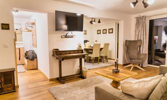 A cozy living room setup with a sofa, a table, and a television. In the background, there is a dining table with chairs and an easily accessible space visible.