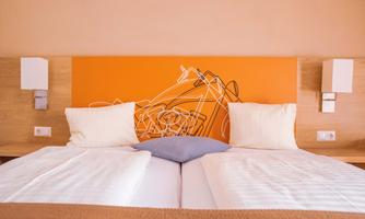 A cozy bed with two pillows and a decorative headboard in orange. The walls are kept neutral, creating a relaxing atmosphere.