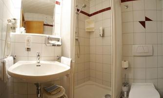 A small bathroom with a shower and a sink. White tiles and a toilet are also included.
