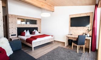 A modern bedroom with a large bed and red accents. There is a desk and a television on the wall.