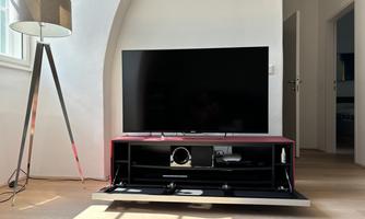A modern living room with a large television on a red TV stand. Next to the television is an elegant floor lamp.
