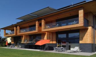 A modern wooden house with large windows and terraces. The surroundings are green and offer a beautiful view.