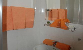 A modern bathroom with a sink and a large mirror. Orange towels complement the decor.