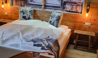 A cozy bedroom with a wooden bed and rustic decoration. On the wall, there is a large picture of a window that creates a rural atmosphere.