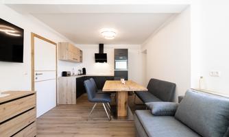 A modernly furnished living space with a dining table, a couch, and a kitchenette. The bright environment creates an inviting atmosphere.