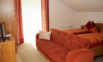 A cozy room with a red sofa and a large window. The walls are light, and the bedding has a striped pattern.