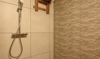 A modern shower with a handy showerhead and a wooden stool. The walls are designed with stylish tiles.