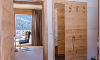 A bright entrance area with wood paneling and a bathroom. Through the window, there is a view of the mountains.