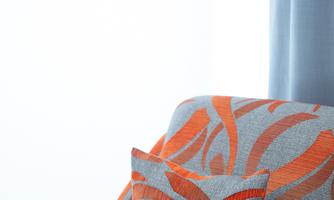 A cozy armchair with a colorful fabric pattern in gray and orange. A matching cushion adorns the seat.