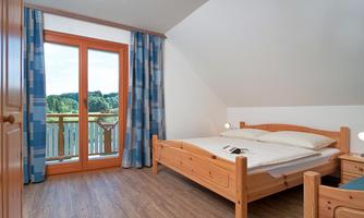 An inviting bedroom with a wooden bed and a large balcony door. A green landscape is visible through the window.