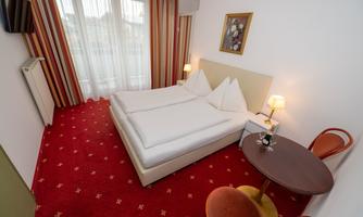 A bright hotel room with two single beds and a small table. The walls are decorated with attractive curtains and a red carpet.