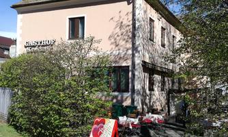 An inn with a bright facade paint and a well-kept garden. Outdoor tables invite you to linger.