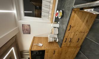 A modern kitchen with wooden cabinets and a black workspace. On the countertop, there is a coffee machine and a fruit bowl.