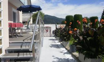 A beautiful outdoor area with tiered access and colorful flower beds. In the background, a mountain landscape and a blue sky can be seen.
