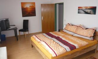 A cozy bedroom with a large bed and bright colors. Pictures hang on the wall, and there is a desk with a chair.