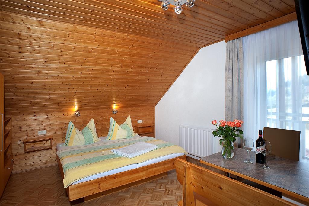 A cozy bedroom with a wooden ceiling and two beds. On the table, there are flowers and a bottle of wine.
