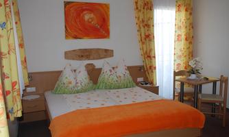 A cozy bedroom with a large bed and colorful pillows. The walls are decorated with light curtains and a painting.