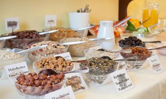 An attractively decorated breakfast counter with various bowls full of nuts, oats, and dried fruits. Next to the bowls are labels with the names of the foods.