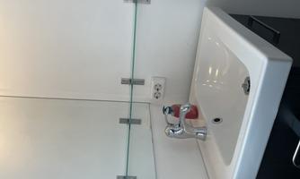 A modern bathroom with a white sink and a large mirror. The walls are light and the faucet is shiny.