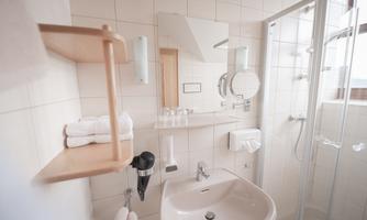 A modern bathroom with a glass shower and a sink. White tiles and wooden shelves create a bright, friendly atmosphere.