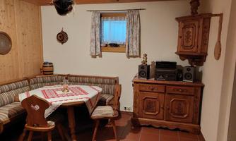 A cozy room with a wooden bench and a table, decorated with a tablecloth. An old cabinet with speakers stands against the wall.